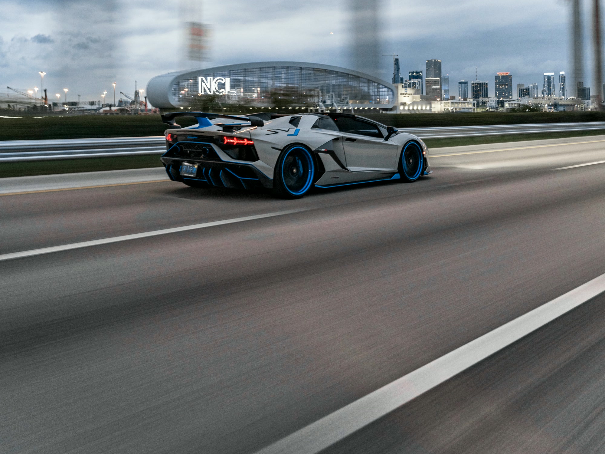 Lamborghini Aventador SVJ in Avery Dennison Gloss Light Grey with gloss blue accents, rolling past the Miami skyline, wrapped by Glass House Wraps